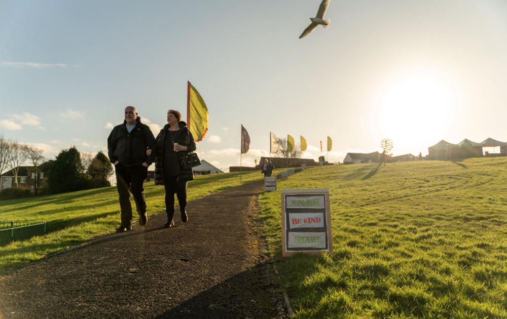 Looking up to the top of Millom Park as visitors walk down the path and flags fly in the background.