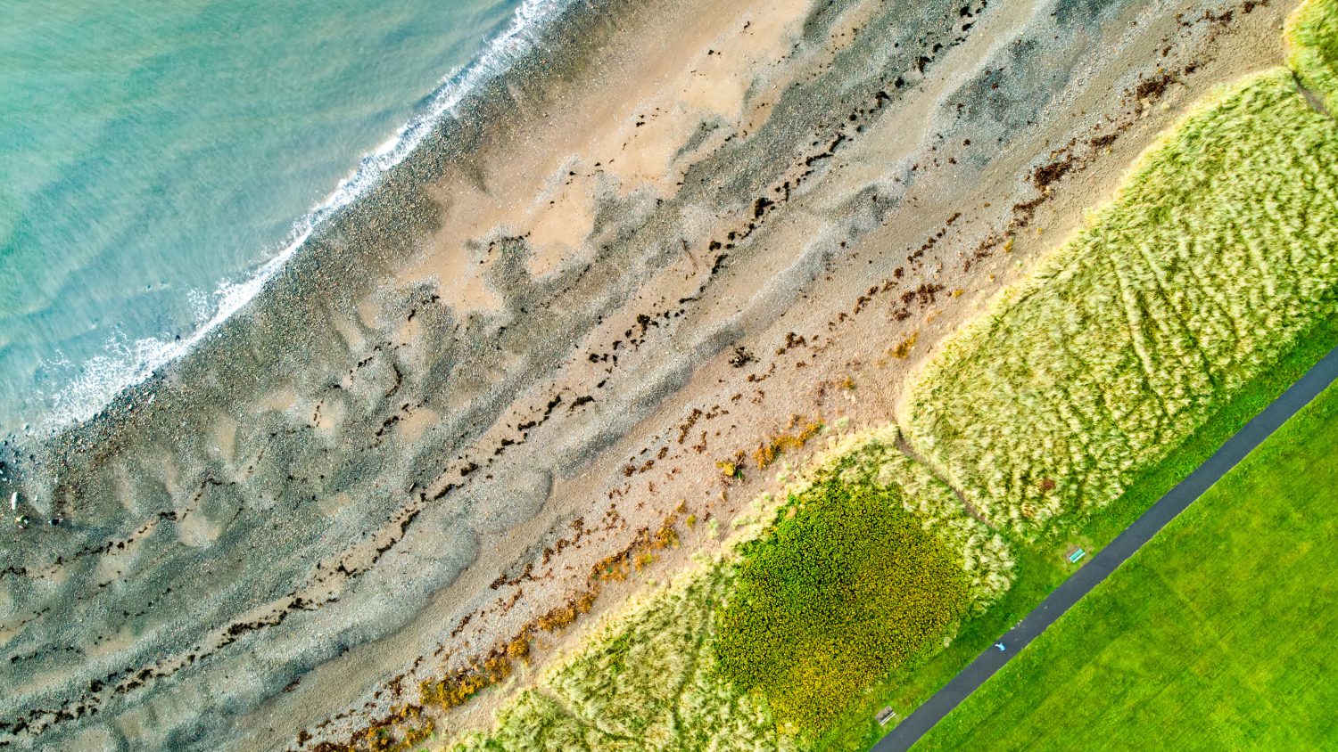 Aerial top-down view of a beach in Allerdale district in Cumbria, UK. Pebble shore of Allonby bay and endless green pastures on autumn evening.